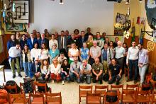 Group Picture and the Wind Energy Workshop, a large group of people standing next to eath other in a toom with some wooden chairs and decoration dangling from the ceiling