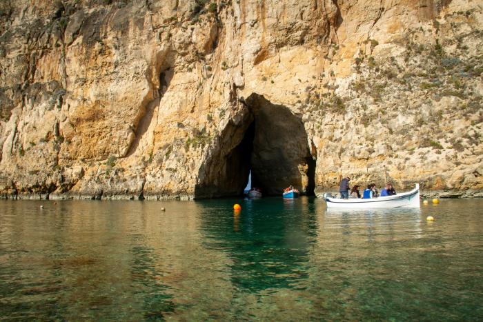cave by the sea with little white boat and people